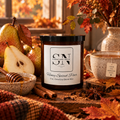 A jar candle labeled 'Honey Spiced Pear' by Signature Note Candle Co. is styled in an autumn scene with pears, cinnamon sticks, a mug of tea, honey, and fall leaves.